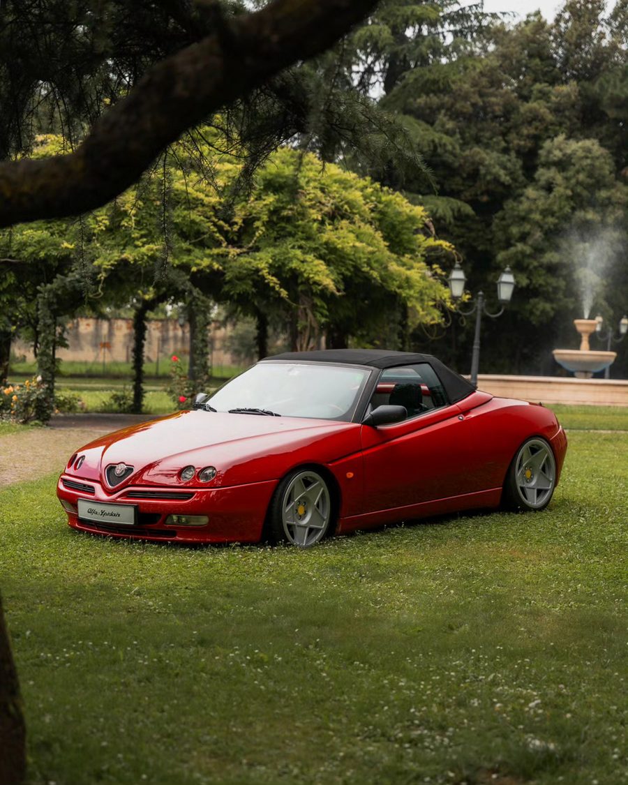 Un'Alfa Romeo Spider rossa sul prato, con una fontana sullo sfondo