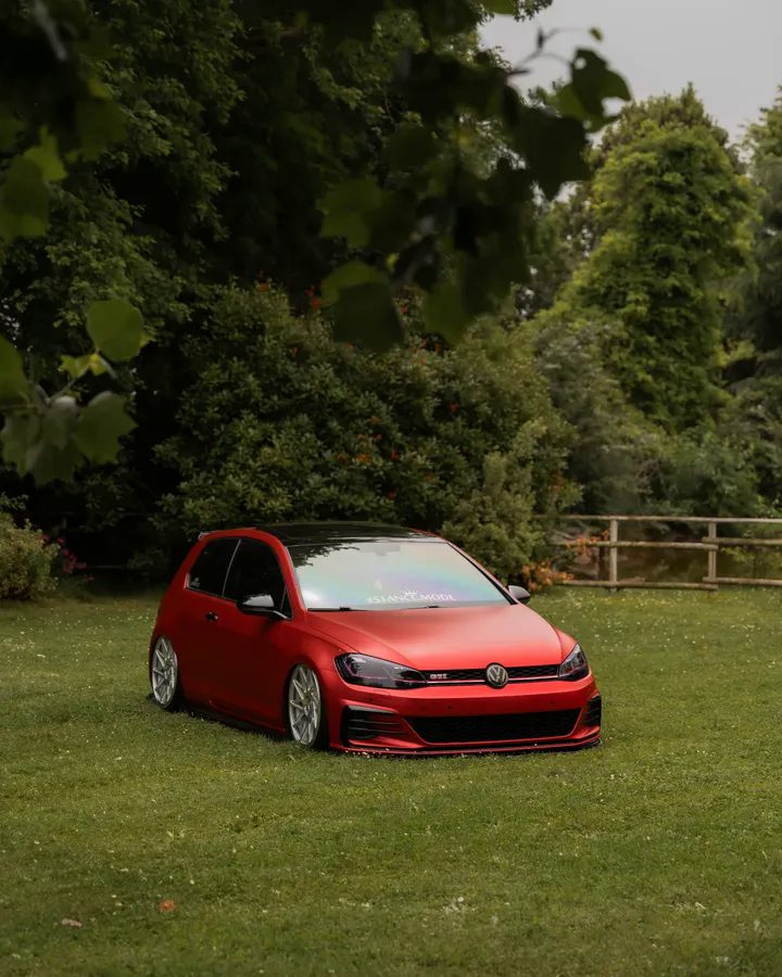 Una Volkswagen Golf GTI rossa ribassata sul prato, davanti al bosco