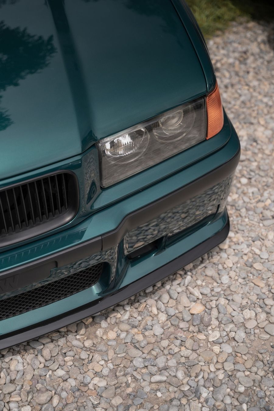 Il frontale di una BMW E36 verde petrolio su ghiaia chiara