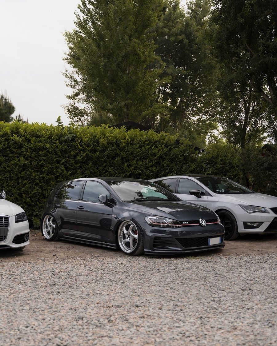 Una Volkswagen Golf grigia ribassata sulla ghiaia, tra le altre auto del raduno