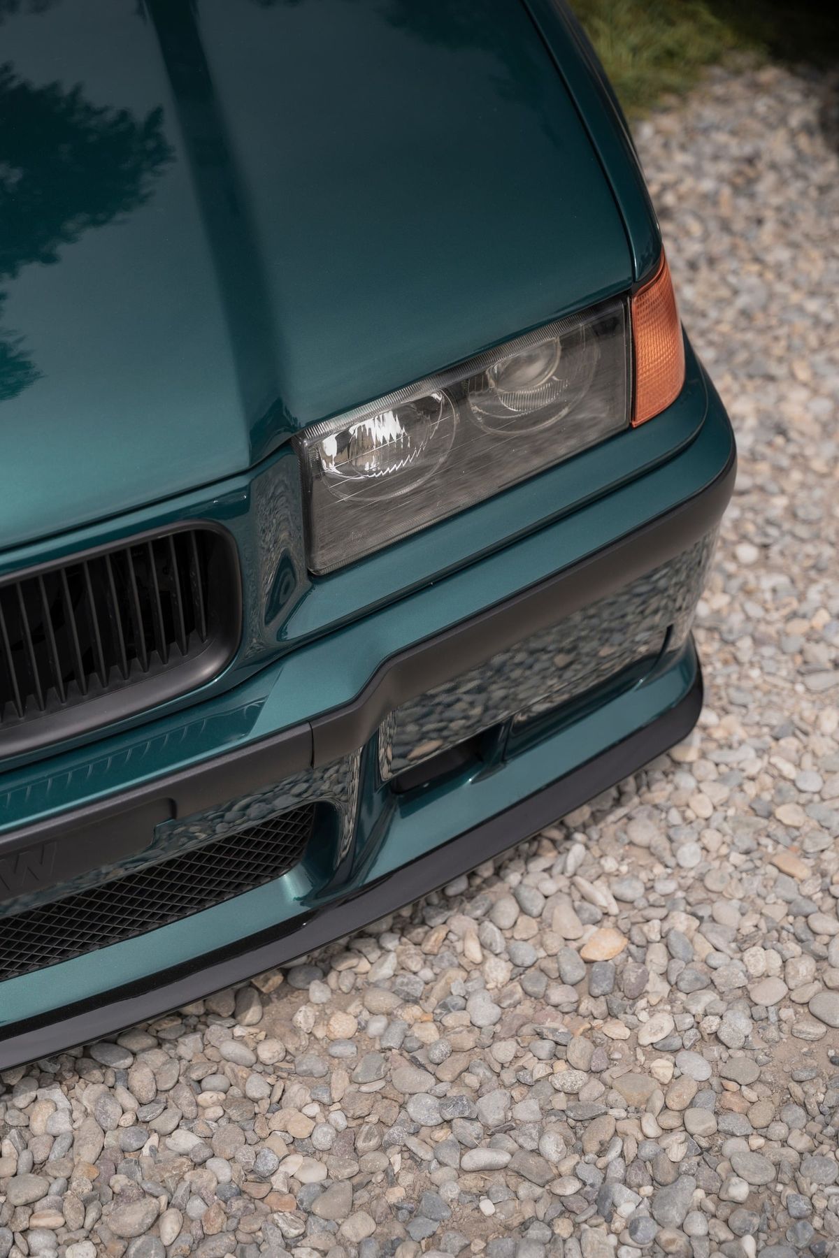 Il frontale di una BMW E36 verde petrolio su ghiaia chiara