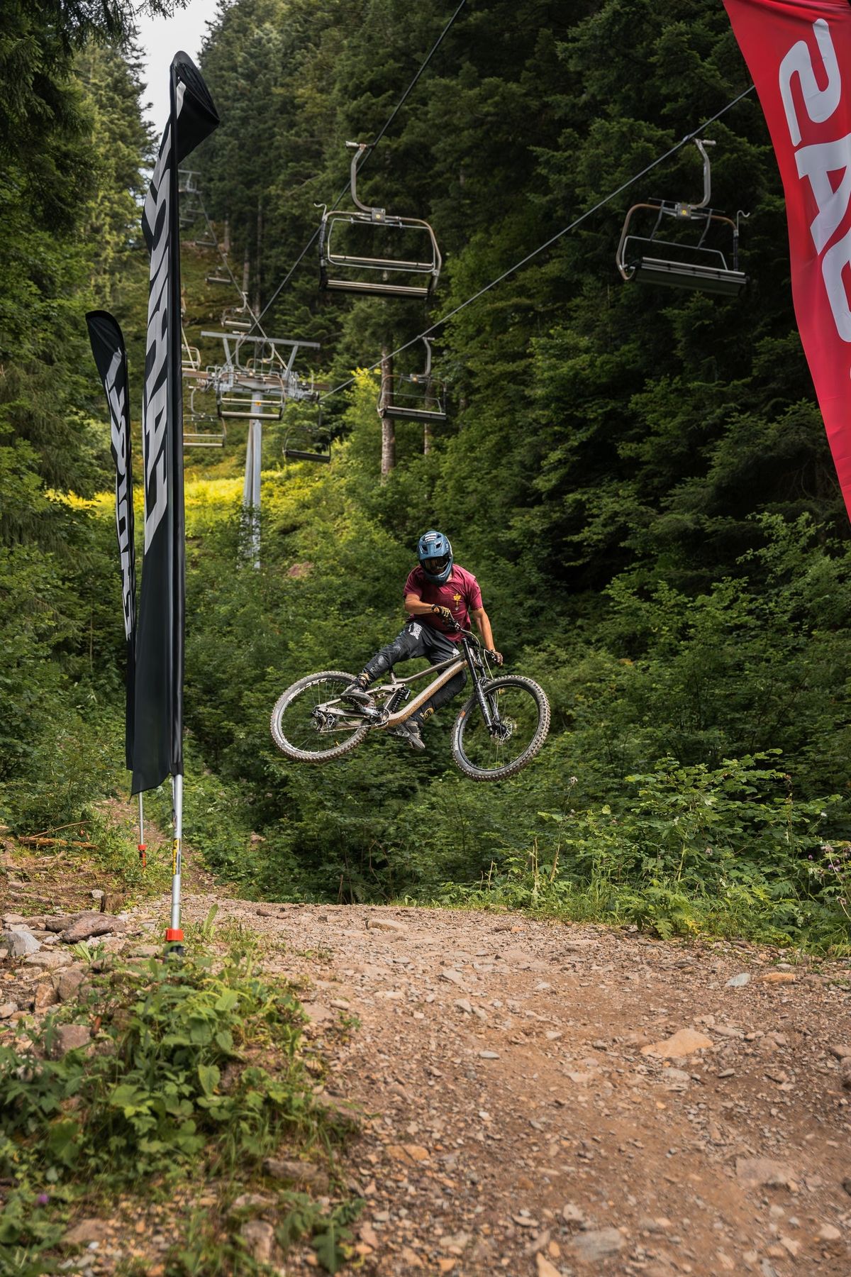 Un biker in salto su un sentiero di downhill nel bosco, sotto la seggiovia