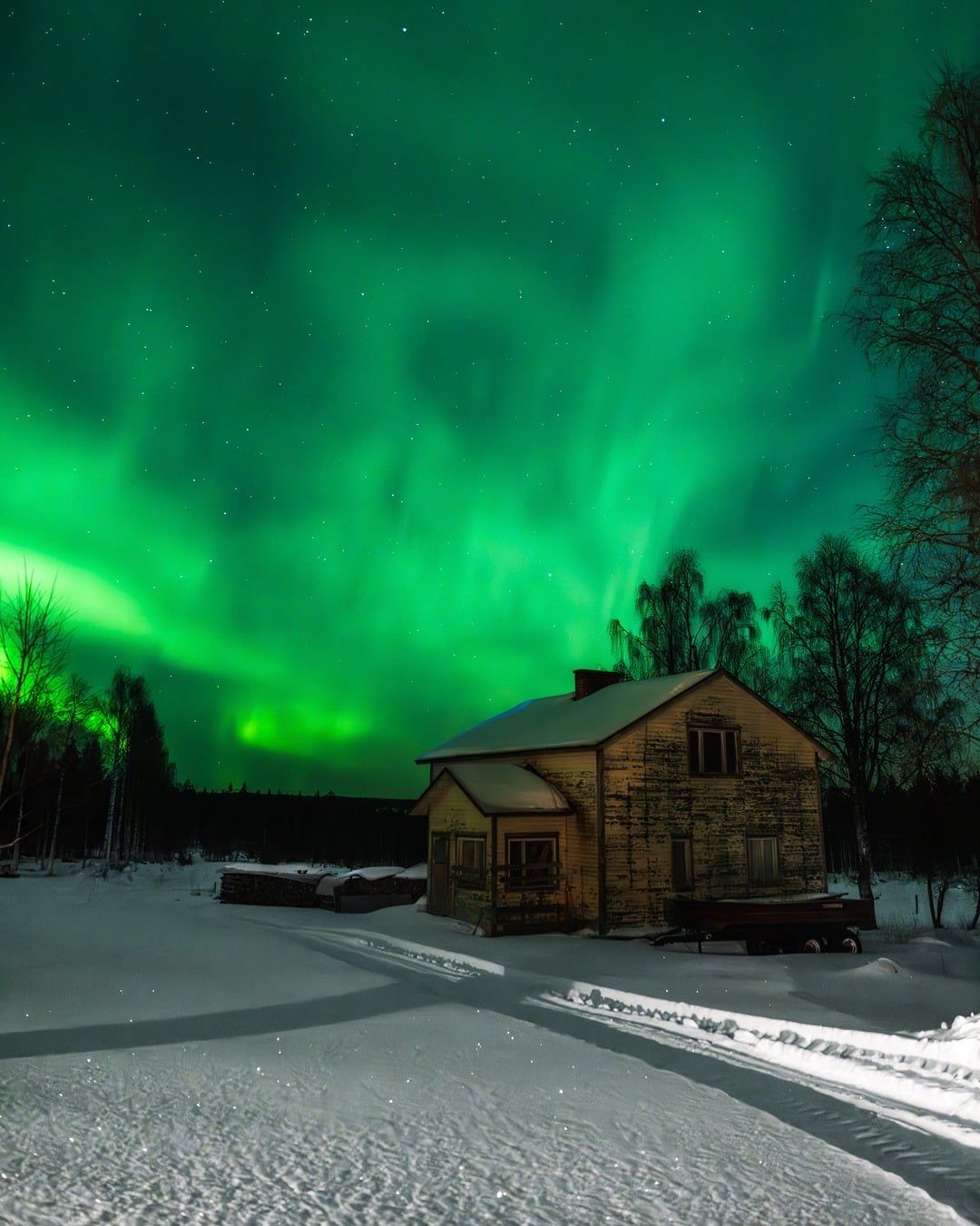 Aurora boreale verde sopra una baita di legno nella neve, in Lapponia
