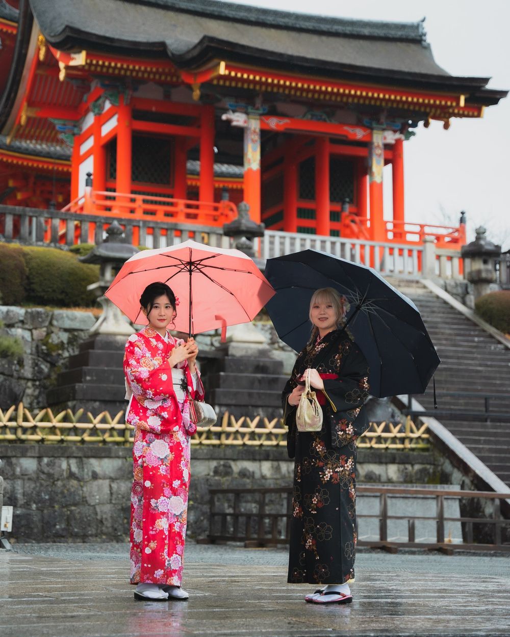 Due ragazze in kimono con gli ombrelli davanti a un tempio rosso, a Kyoto, foto di Thomas Peccati