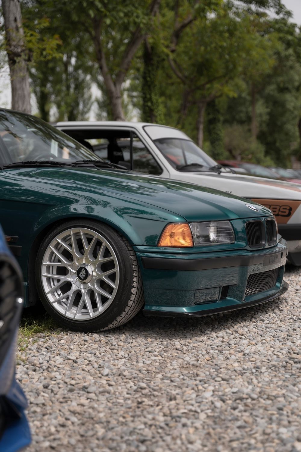 Una BMW E36 verde petrolio ribassata sul prato, davanti al verde