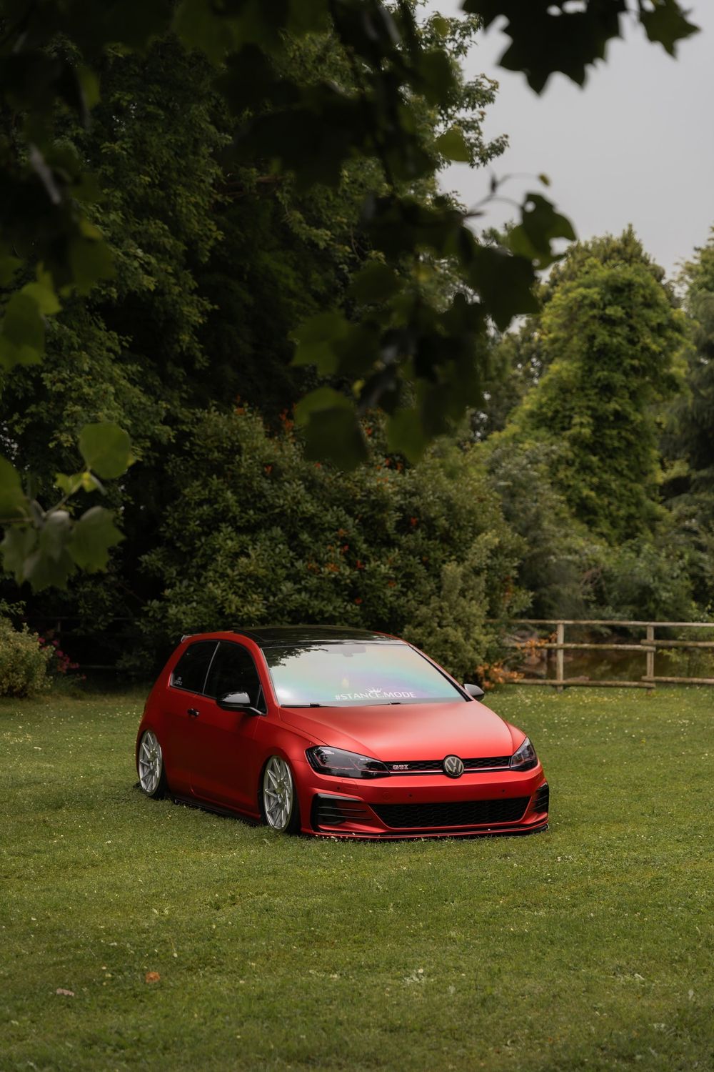 Una Volkswagen Golf rossa ribassata su un prato, nel verde di un parco