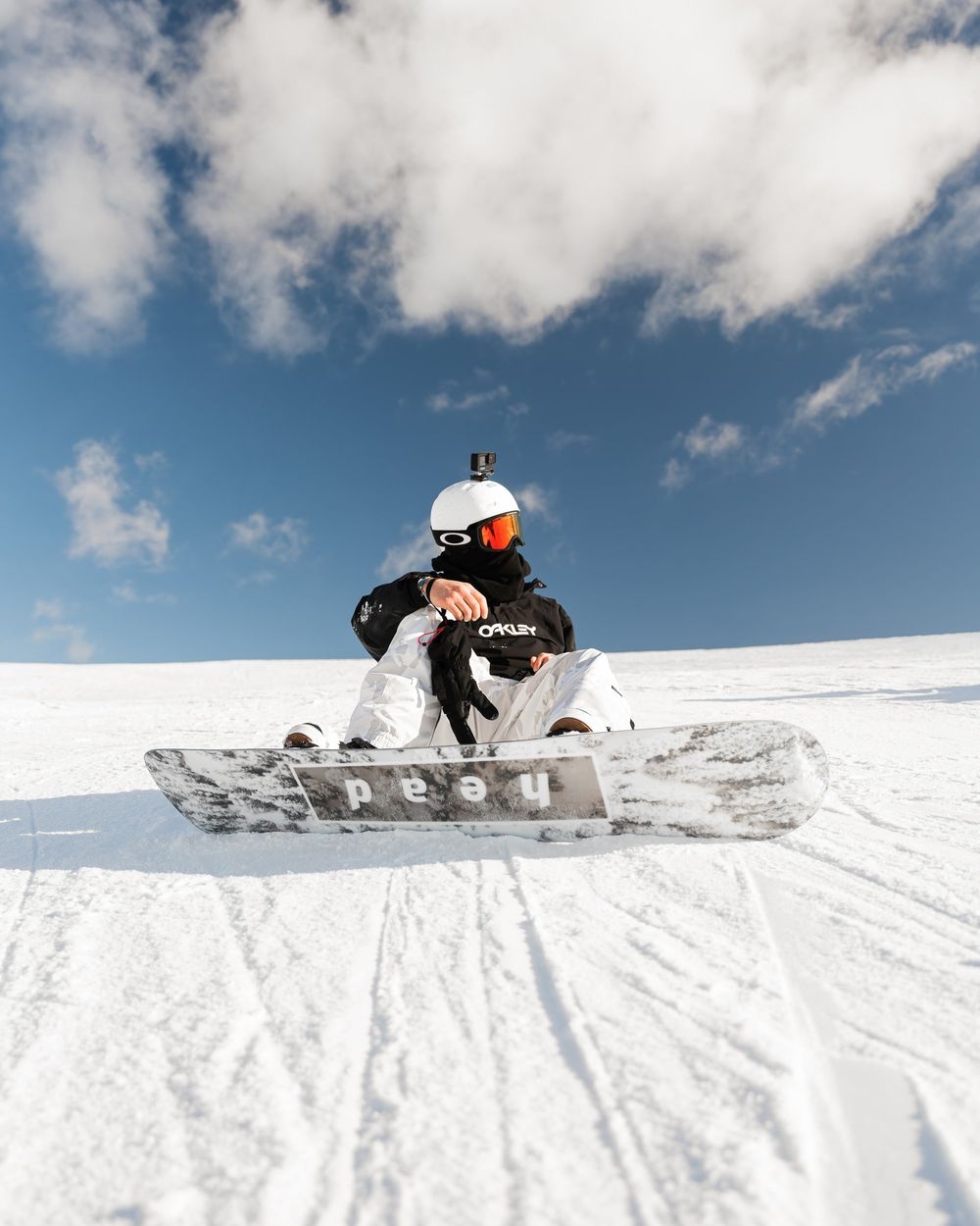 Uno snowboarder seduto sulla neve, sotto un cielo blu con le nuvole