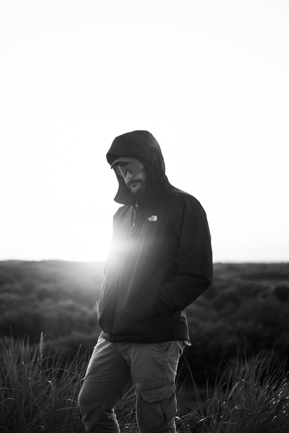Thomas Peccati con il cappuccio, controluce, in un prato al tramonto, in bianco e nero